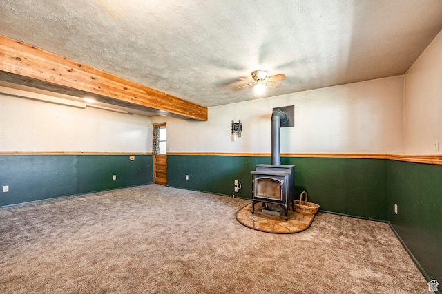 below grade area with a wood stove, carpet floors, a ceiling fan, baseboards, and a textured ceiling