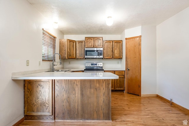 kitchen featuring appliances with stainless steel finishes, a sink, light wood-type flooring, light countertops, and brown cabinetry