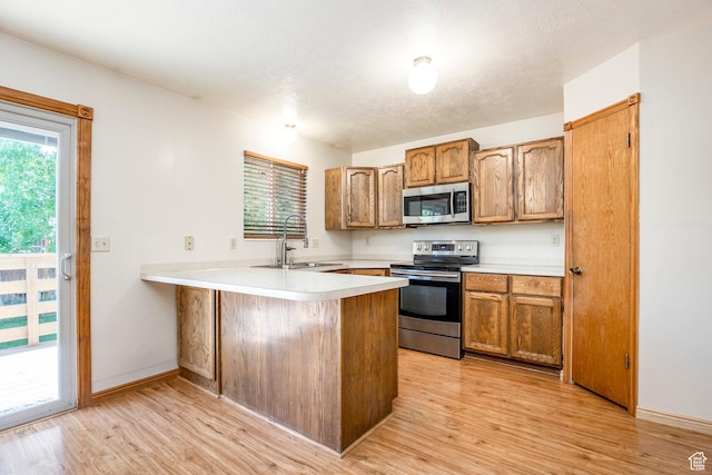 kitchen with stainless steel appliances, a sink, a peninsula, light countertops, and light wood-style flooring