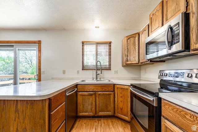 kitchen with appliances with stainless steel finishes, a sink, a peninsula, healthy amount of natural light, and a textured ceiling