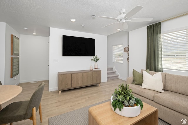 living room featuring light wood-style flooring, recessed lighting, baseboards, ceiling fan, and a textured ceiling