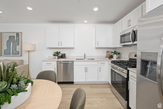 kitchen with stainless steel appliances, a sink, light countertops, white cabinetry, and light wood-type flooring
