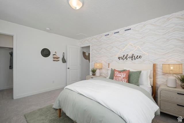 bedroom featuring carpet, baseboards, a walk in closet, a closet, and a textured ceiling
