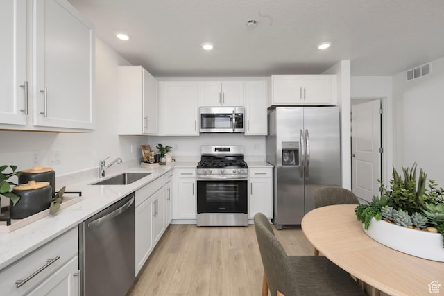 kitchen with stainless steel appliances, a sink, light wood-style flooring, white cabinets, and light stone counters