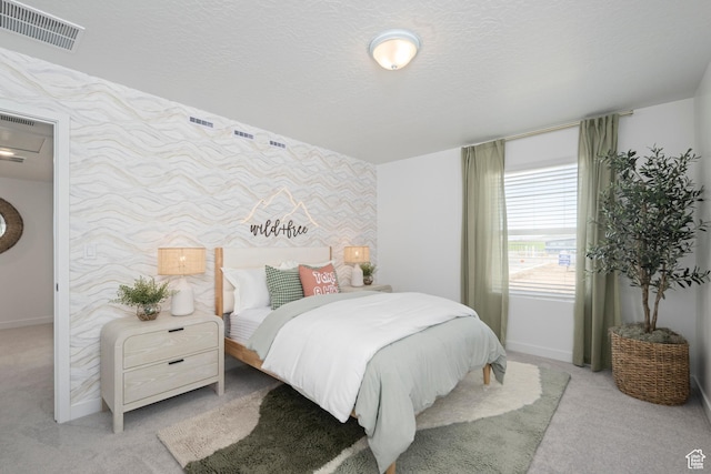 bedroom with an accent wall, wallpapered walls, carpet floors, baseboards, and a textured ceiling