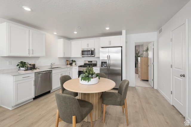 kitchen featuring appliances with stainless steel finishes, a sink, light wood-style floors, white cabinets, and recessed lighting