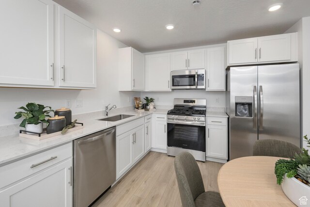 kitchen with stainless steel appliances, a sink, light wood-style flooring, white cabinetry, and recessed lighting