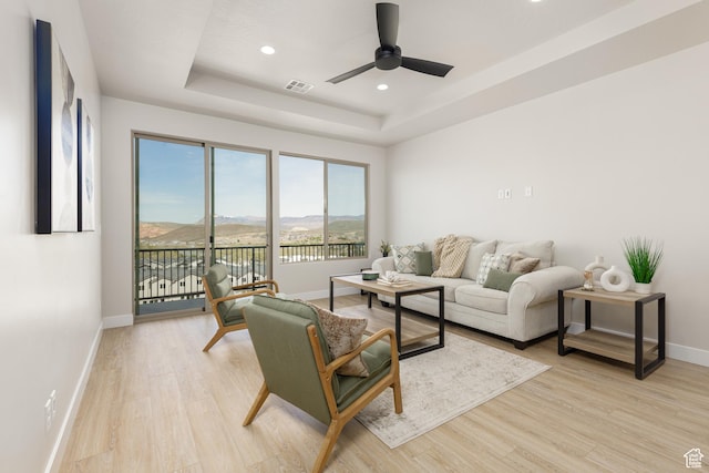 living room featuring a raised ceiling, baseboards, light wood-type flooring, recessed lighting, and ceiling fan