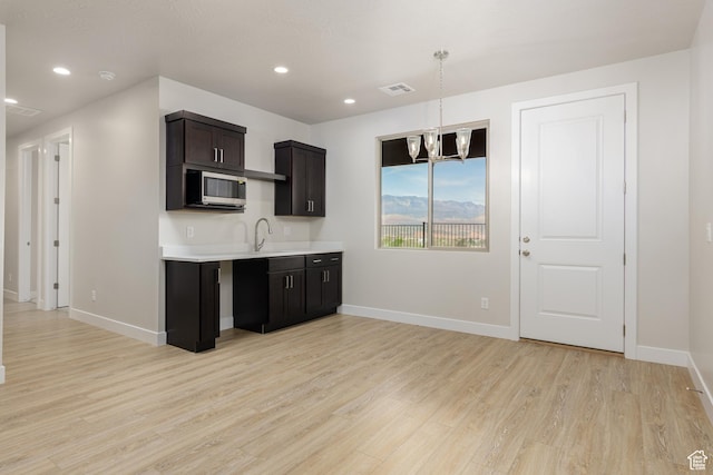 kitchen featuring stainless steel microwave, light countertops, light wood finished floors, baseboards, and recessed lighting