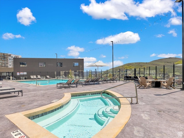 community pool featuring fence, a mountain view, a patio area, and a hot tub