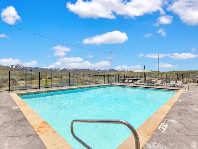 community pool with fence, a mountain view, and a patio area