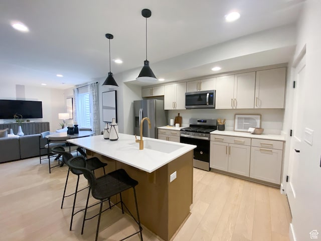 kitchen featuring appliances with stainless steel finishes, a sink, light wood-type flooring, recessed lighting, and a kitchen breakfast bar