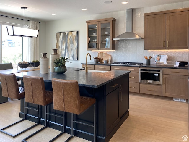 kitchen with wall chimney exhaust hood, stainless steel appliances, a sink, a kitchen bar, and glass insert cabinets