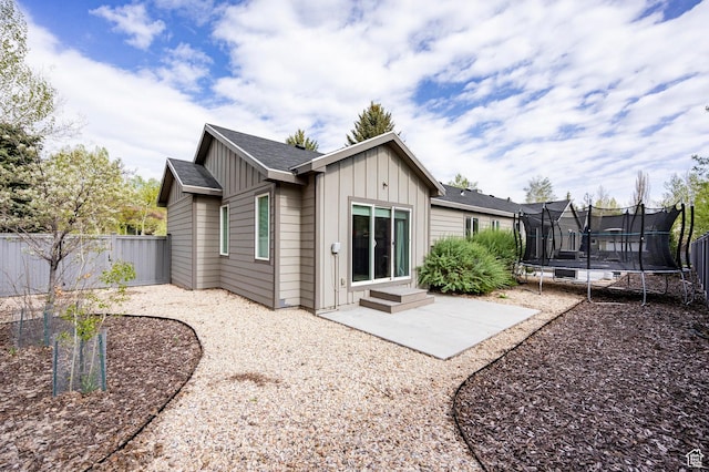 rear view of house featuring a trampoline, board and batten siding, a patio, and a fenced backyard