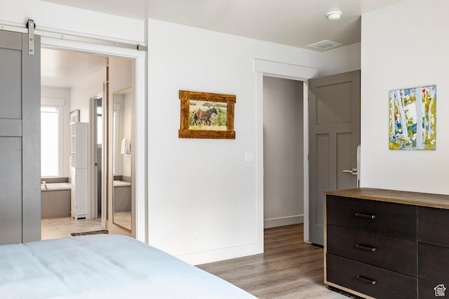 bedroom featuring light wood finished floors, ensuite bathroom, and baseboards
