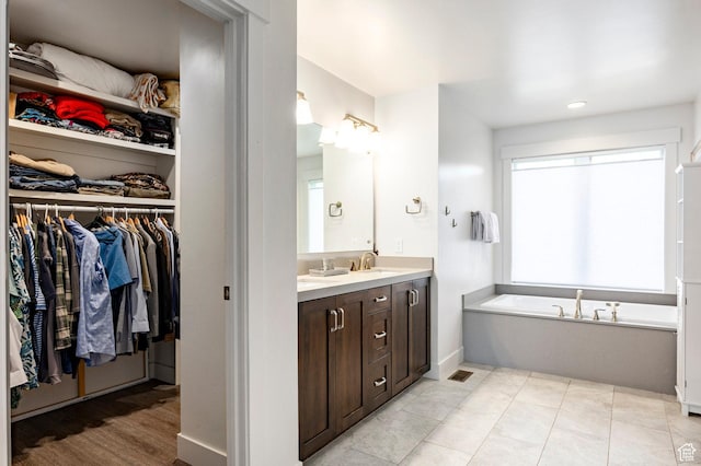 bathroom featuring vanity, a walk in closet, a garden tub, recessed lighting, and baseboards