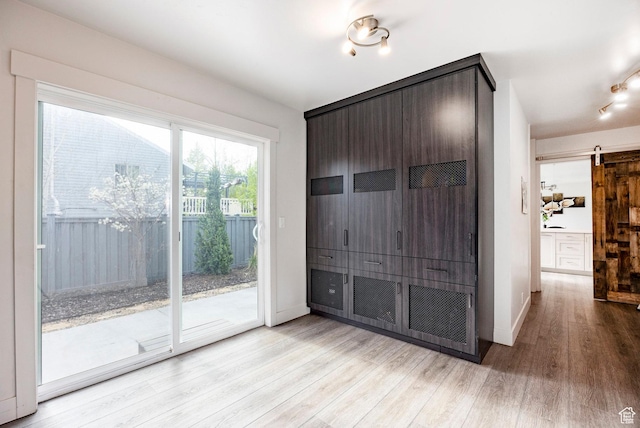 empty room featuring light wood finished floors, a barn door, and baseboards