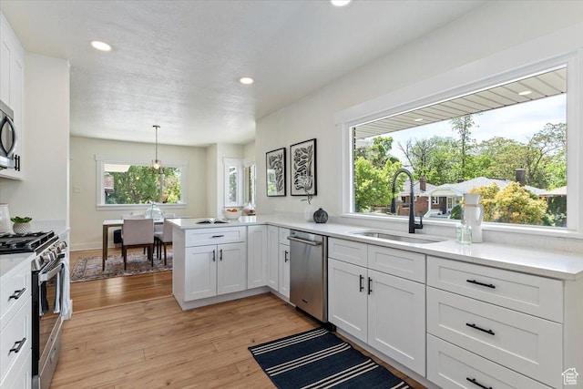 kitchen featuring appliances with stainless steel finishes, a sink, white cabinets, a peninsula, and recessed lighting
