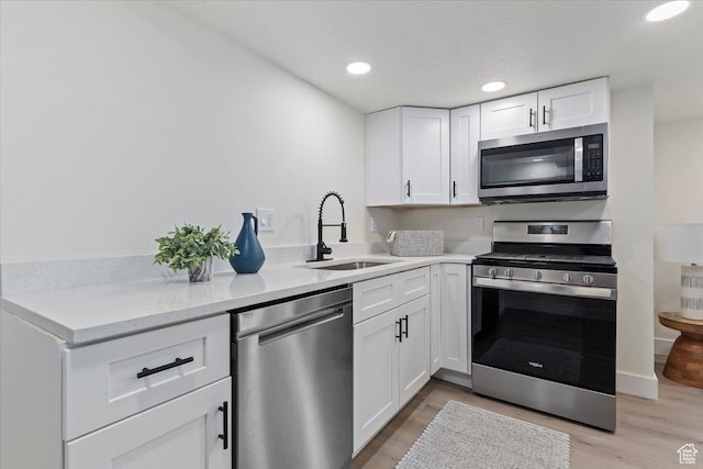 kitchen with appliances with stainless steel finishes, a sink, white cabinets, light wood-style floors, and recessed lighting