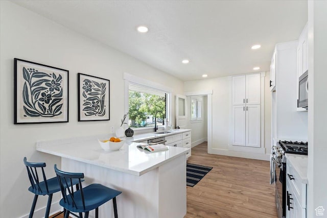 kitchen featuring stainless steel appliances, a peninsula, a breakfast bar area, a sink, and white cabinets