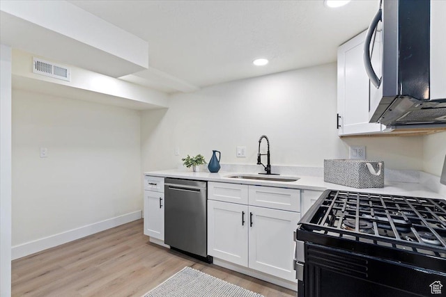 kitchen featuring stainless steel dishwasher, a sink, white cabinets, light wood-type flooring, and recessed lighting