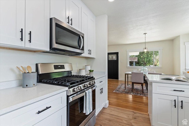 kitchen featuring appliances with stainless steel finishes, light wood-type flooring, light countertops, white cabinets, and a textured ceiling