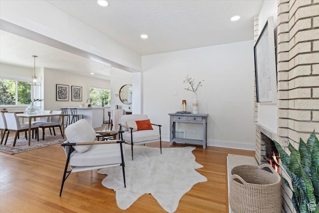 living area with light wood-style flooring, a brick fireplace, recessed lighting, and baseboards