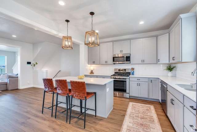 kitchen with appliances with stainless steel finishes, a sink, a kitchen bar, a chandelier, and light wood-style floors