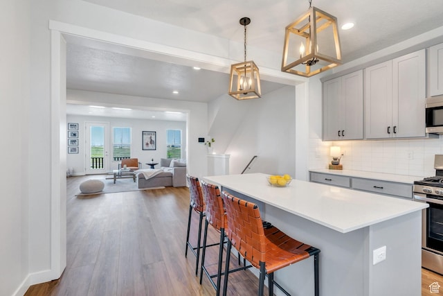 kitchen featuring stainless steel appliances, a kitchen island, light countertops, backsplash, and wood finished floors