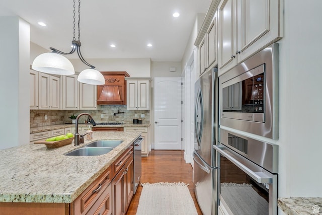 kitchen featuring appliances with stainless steel finishes, a sink, backsplash, dark wood-style floors, and light stone counters