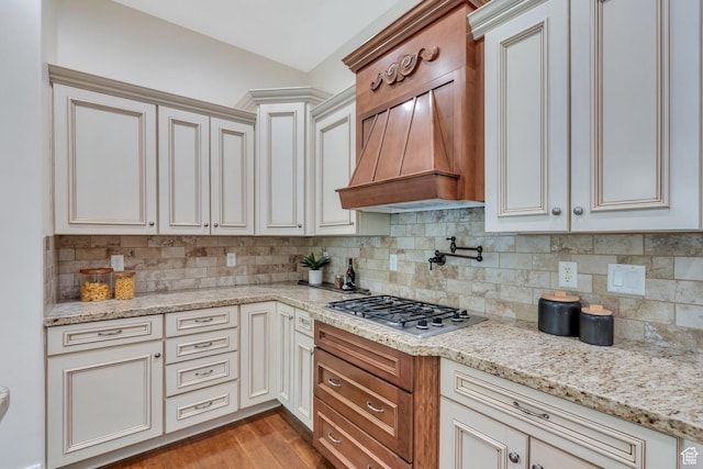 kitchen featuring stainless steel gas cooktop, backsplash, light stone countertops, light wood-style floors, and custom exhaust hood