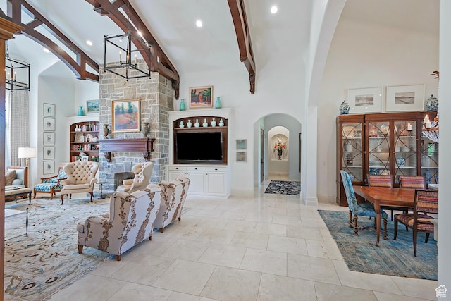 living room with a chandelier, beam ceiling, arched walkways, high vaulted ceiling, and a stone fireplace