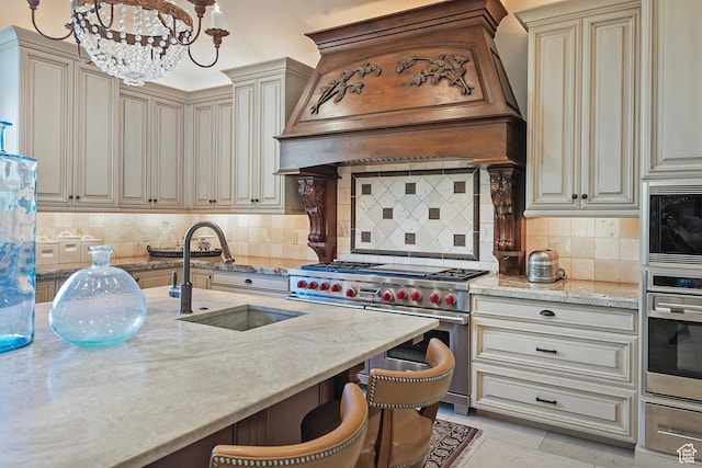 kitchen featuring appliances with stainless steel finishes, a sink, custom range hood, light stone counters, and cream cabinets