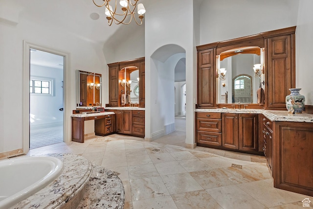 bathroom with a chandelier, a towering ceiling, baseboards, a garden tub, and two vanities