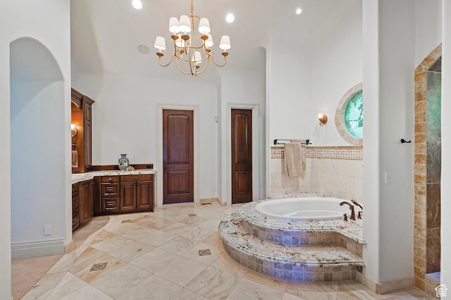 bathroom featuring a towering ceiling, a garden tub, vanity, a chandelier, and baseboards