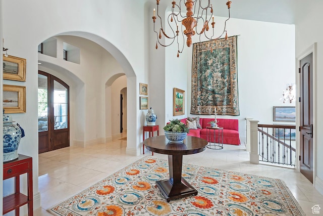 foyer with light tile patterned floors, a towering ceiling, a chandelier, arched walkways, and baseboards