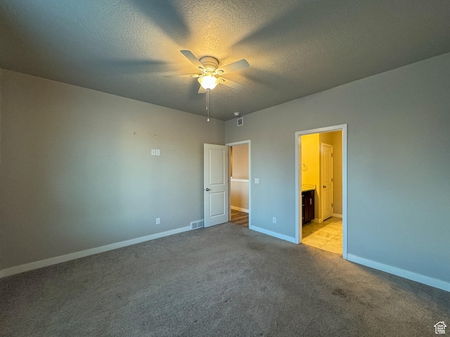 unfurnished bedroom featuring baseboards, light carpet, a textured ceiling, ceiling fan, and ensuite bath