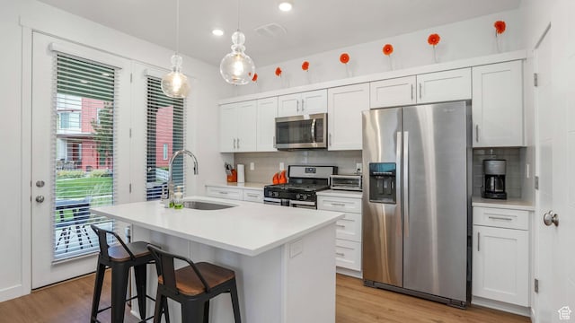 kitchen with stainless steel appliances, a sink, a kitchen island with sink, decorative backsplash, and light wood-type flooring