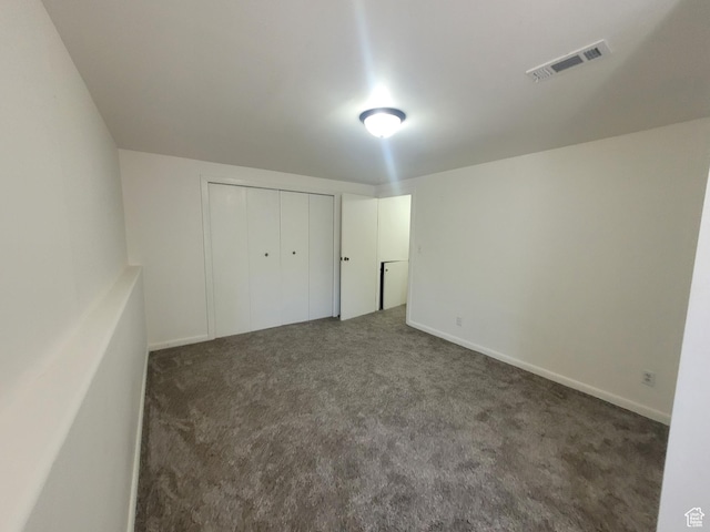 unfurnished bedroom featuring dark carpet and a closet