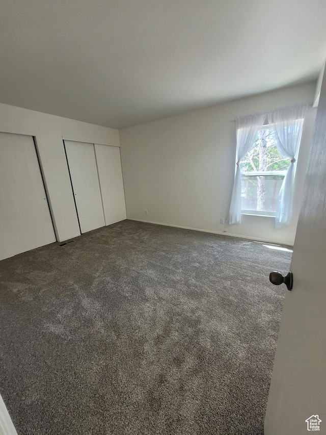 unfurnished bedroom featuring dark carpet and multiple closets