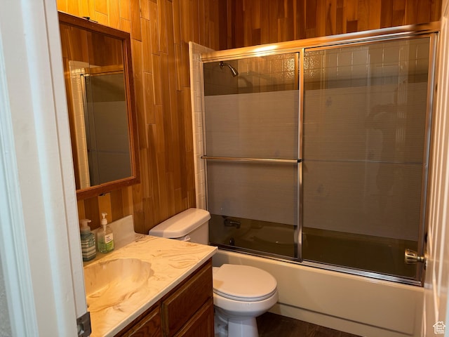 full bathroom with wood walls, toilet, shower / bath combination with glass door, and vanity