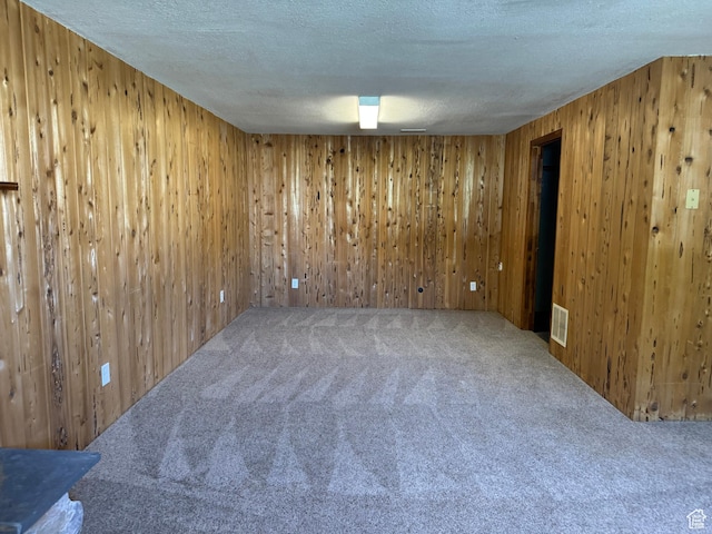 carpeted spare room with a textured ceiling and wooden walls
