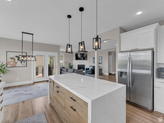 kitchen featuring stainless steel fridge with ice dispenser, a kitchen island, a fireplace, light wood-style floors, and light stone countertops