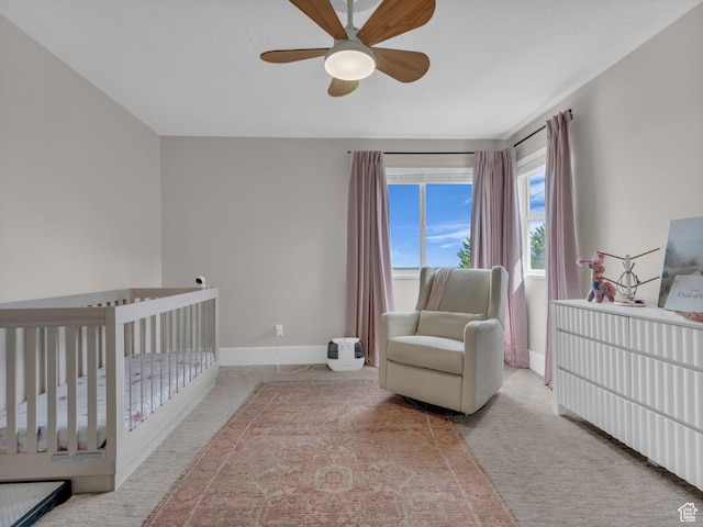 bedroom with a crib, baseboards, carpet flooring, and ceiling fan