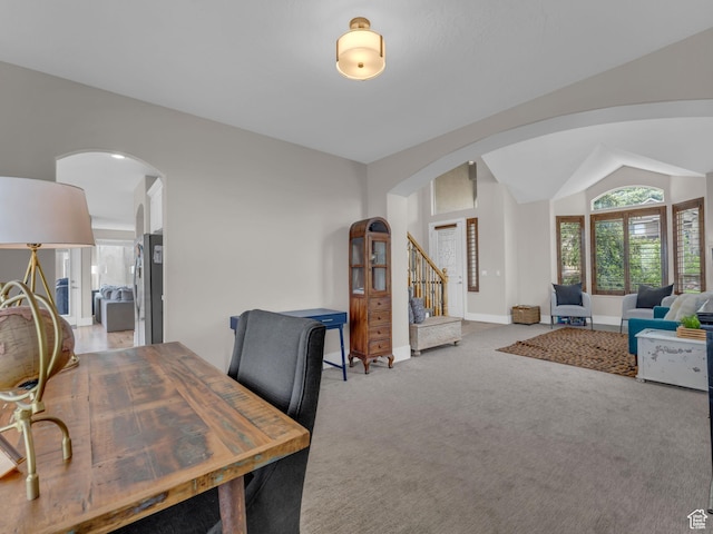 home office featuring arched walkways, light colored carpet, baseboards, and vaulted ceiling