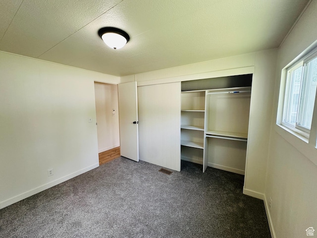 unfurnished bedroom featuring carpet flooring, a closet, a textured ceiling, and baseboards
