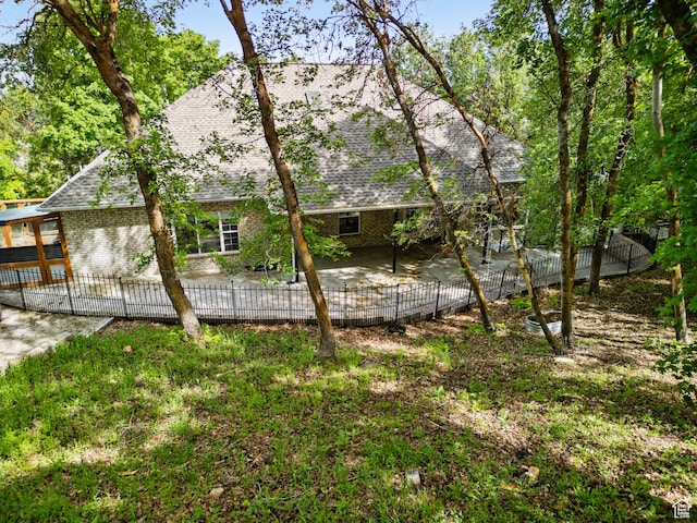 rear view of house featuring a patio area, a shingled roof, brick siding, and a fenced backyard