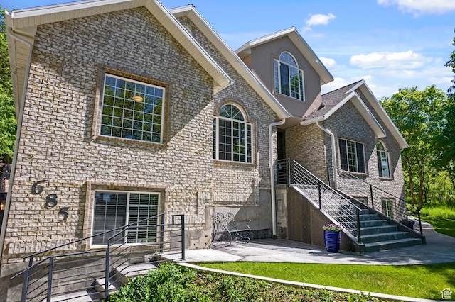 view of front facade with a patio, brick siding, stairway, and stucco siding