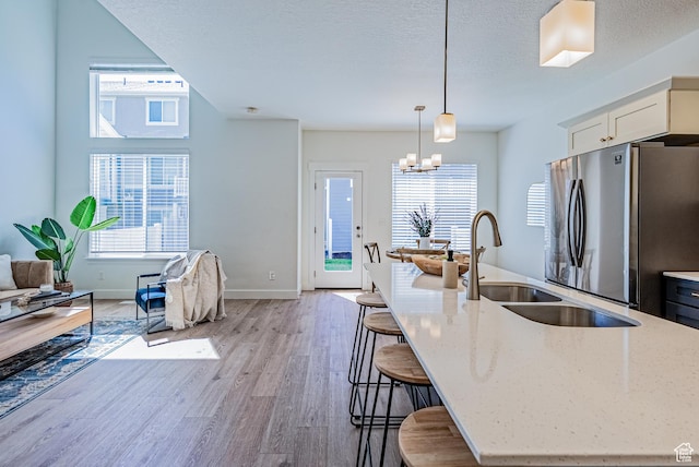 kitchen featuring freestanding refrigerator, light stone counters, light wood-style floors, decorative light fixtures, and a breakfast bar area