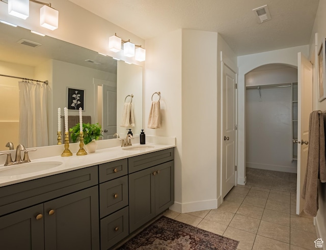 full bathroom featuring tile patterned floors, double vanity, baseboards, and a walk in closet